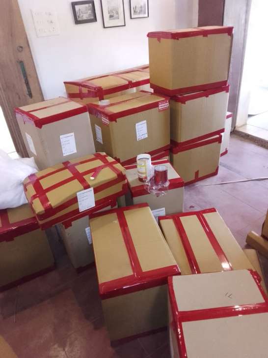 Cardboard cartons sealed with red tape and white labels, stacked in a room.