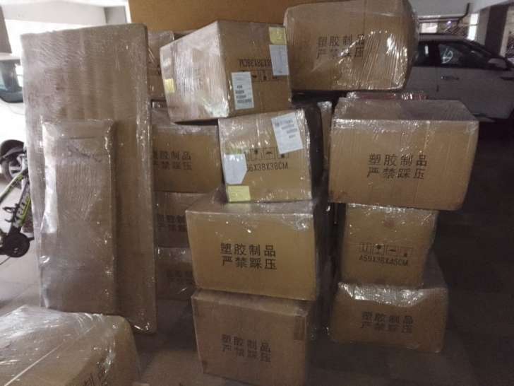 Cardboard cartons wrapped in clear plastic, stacked with a parked car in the background.